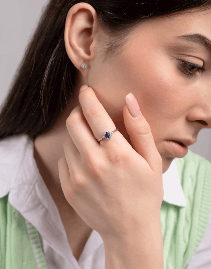 Elegancki pierścionek z szafirem i brylantami noszony przez kobietę w zielonej kamizelce