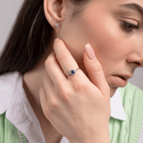 Elegancki pierścionek z szafirem i brylantami noszony przez kobietę w zielonej kamizelce