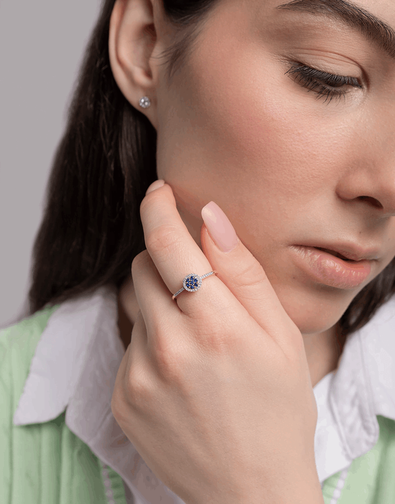 Pierścionek z szafirem i diamentami noszony przez kobietę na eleganckim tle z delikatnym uśmiechem