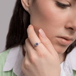 Pierścionek z szafirem i diamentami noszony przez kobietę na eleganckim tle z delikatnym uśmiechem