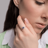 Pierścionek z szafirem i diamentami noszony przez kobietę na eleganckim tle z delikatnym uśmiechem