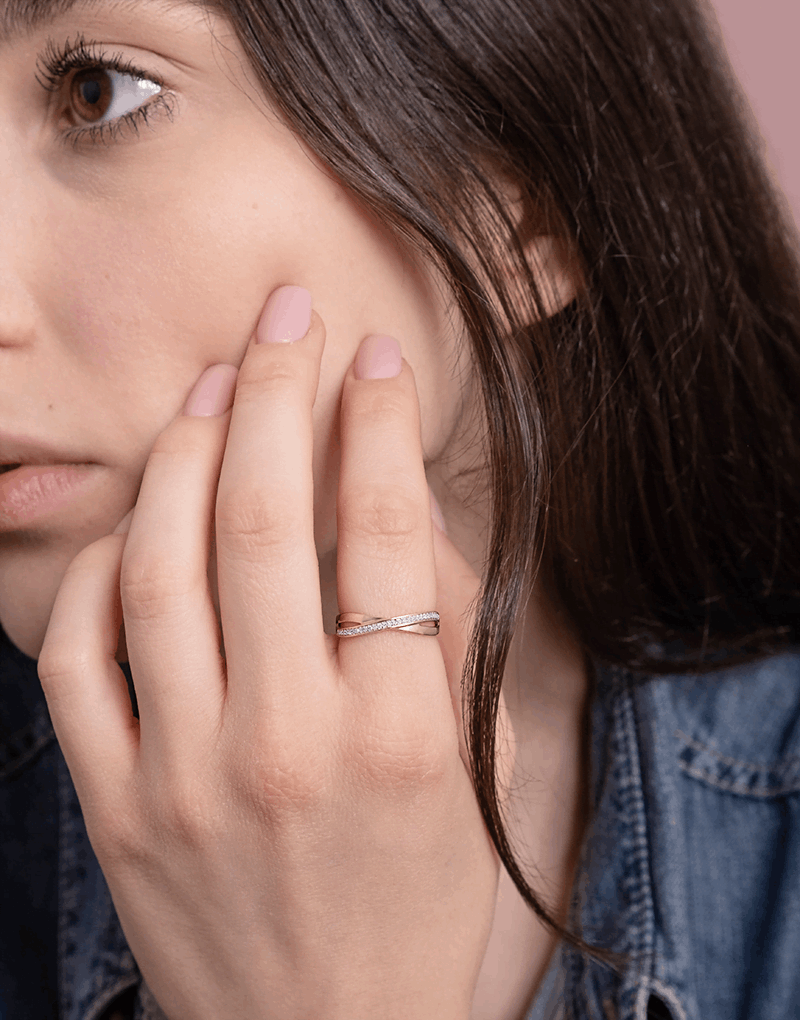 Skręcony pierścionek z brylantami od Venetia Jewels na palcu modelki, w subtelnym otoczeniu