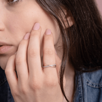 Skręcony pierścionek z brylantami od Venetia Jewels na palcu modelki, w subtelnym otoczeniu