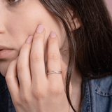 Skręcony pierścionek z brylantami od Venetia Jewels na palcu modelki, w subtelnym otoczeniu