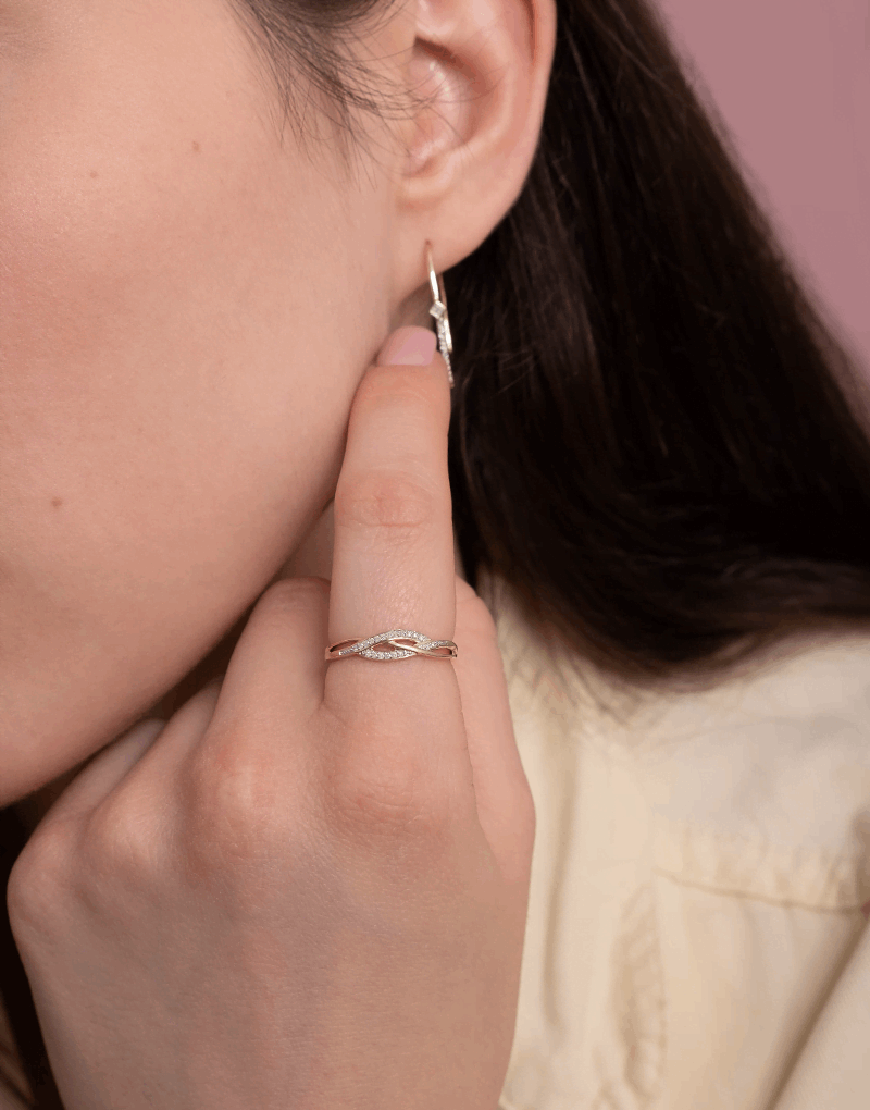 Elegancki spleciony pierścionek z brylantami na palcu, z subtelnymi kolczykami w tle