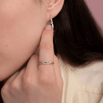 Elegancki spleciony pierścionek z brylantami na palcu, z subtelnymi kolczykami w tle