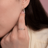 Elegancki spleciony pierścionek z brylantami na palcu, z subtelnymi kolczykami w tle