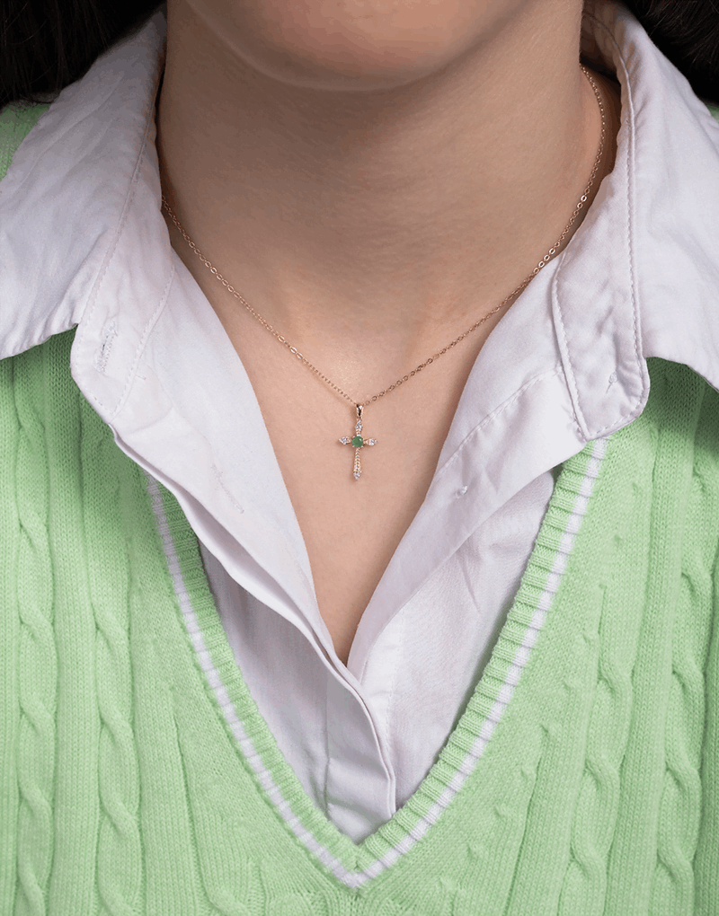 Wisiorek krzyż ze szmaragdem na delikatnym łańcuszku, noszony na szyi przez osobę w zielonym swetrze