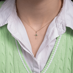 Wisiorek krzyż ze szmaragdem na delikatnym łańcuszku, noszony na szyi przez osobę w zielonym swetrze