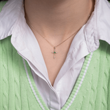 Wisiorek krzyż ze szmaragdem na delikatnym łańcuszku, noszony na szyi przez osobę w zielonym swetrze