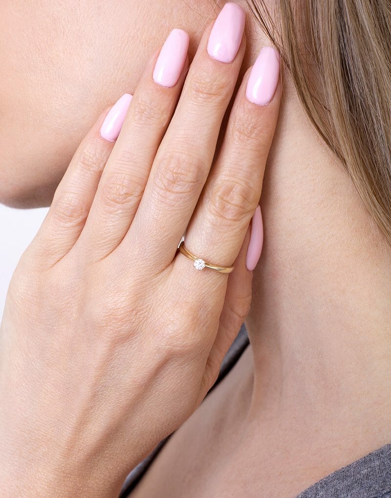 Kobieta nosząca klasyczny pierścionek z brylantem na palcu, w subtelnej stylizacji