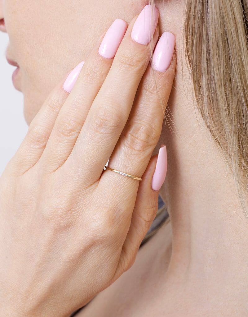 Stylowa smukła obrączka z brylantami noszona na palcu z różowymi paznokciami