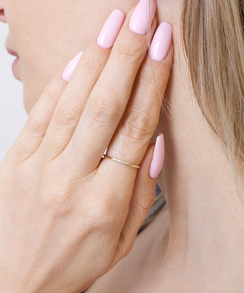 Stylowa smukła obrączka z brylantami noszona na palcu z różowymi paznokciami