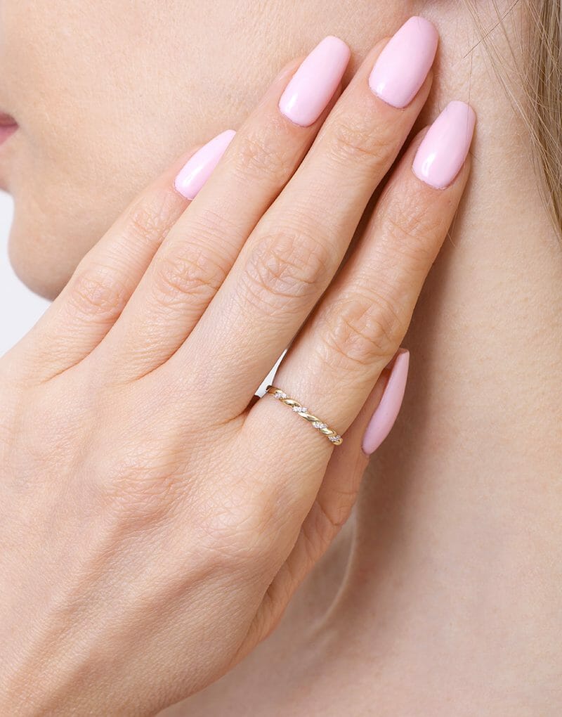 Złota obrączka z brylantami na palcu, pięknie zdobiąca dłoń kobiety z różowymi paznokciami