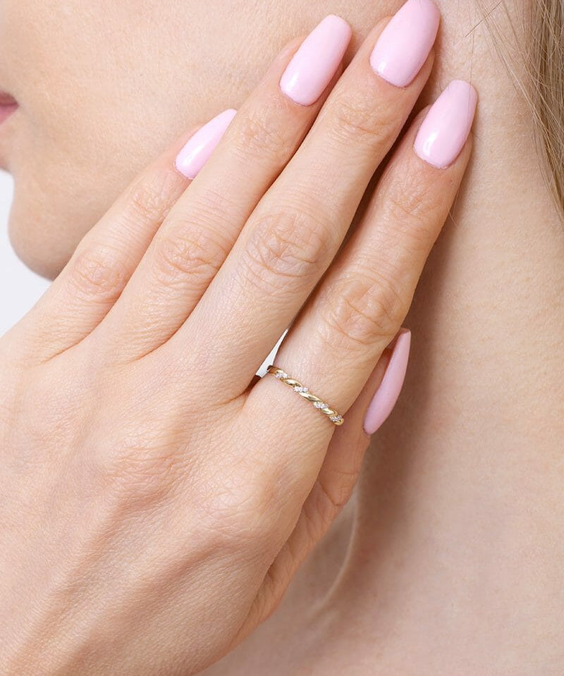 Złota obrączka z brylantami na palcu, pięknie zdobiąca dłoń kobiety z różowymi paznokciami