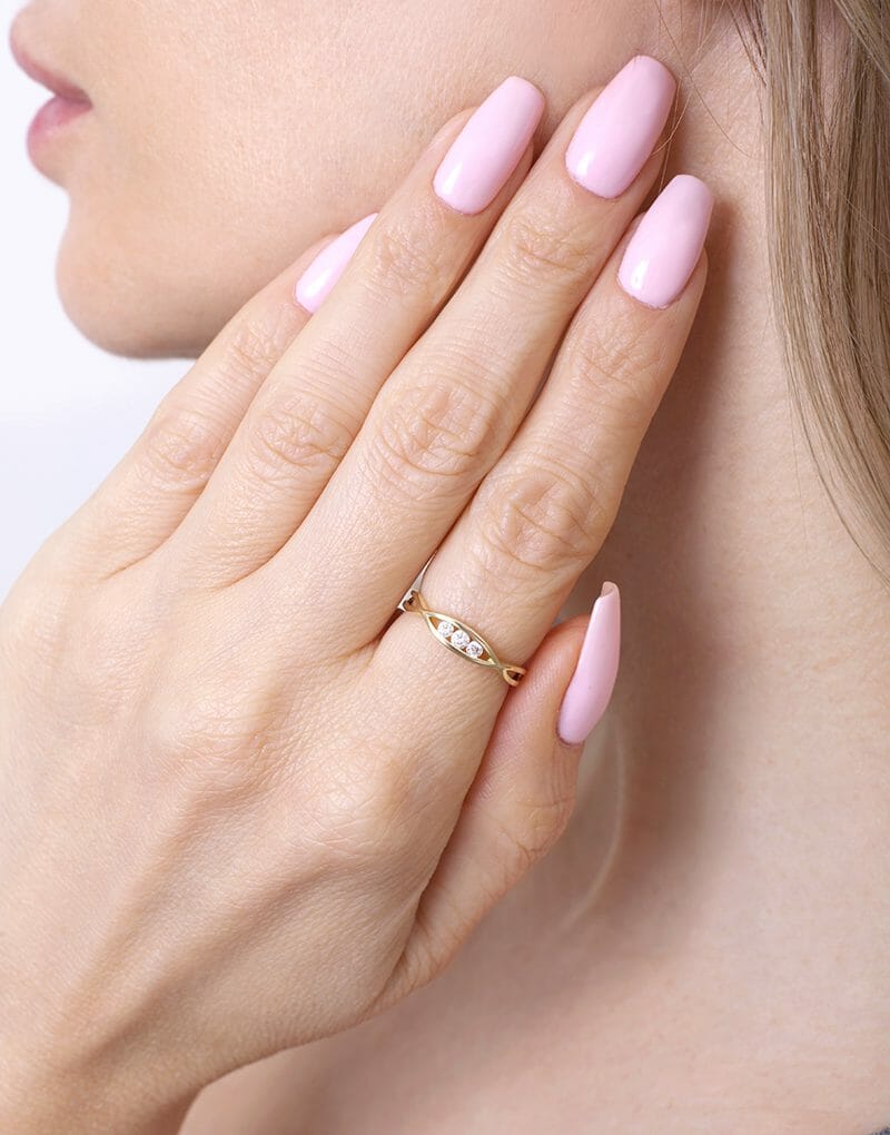 Skręcony złoty pierścionek od Venetia Jewels na dłoni z różowymi paznokciami
