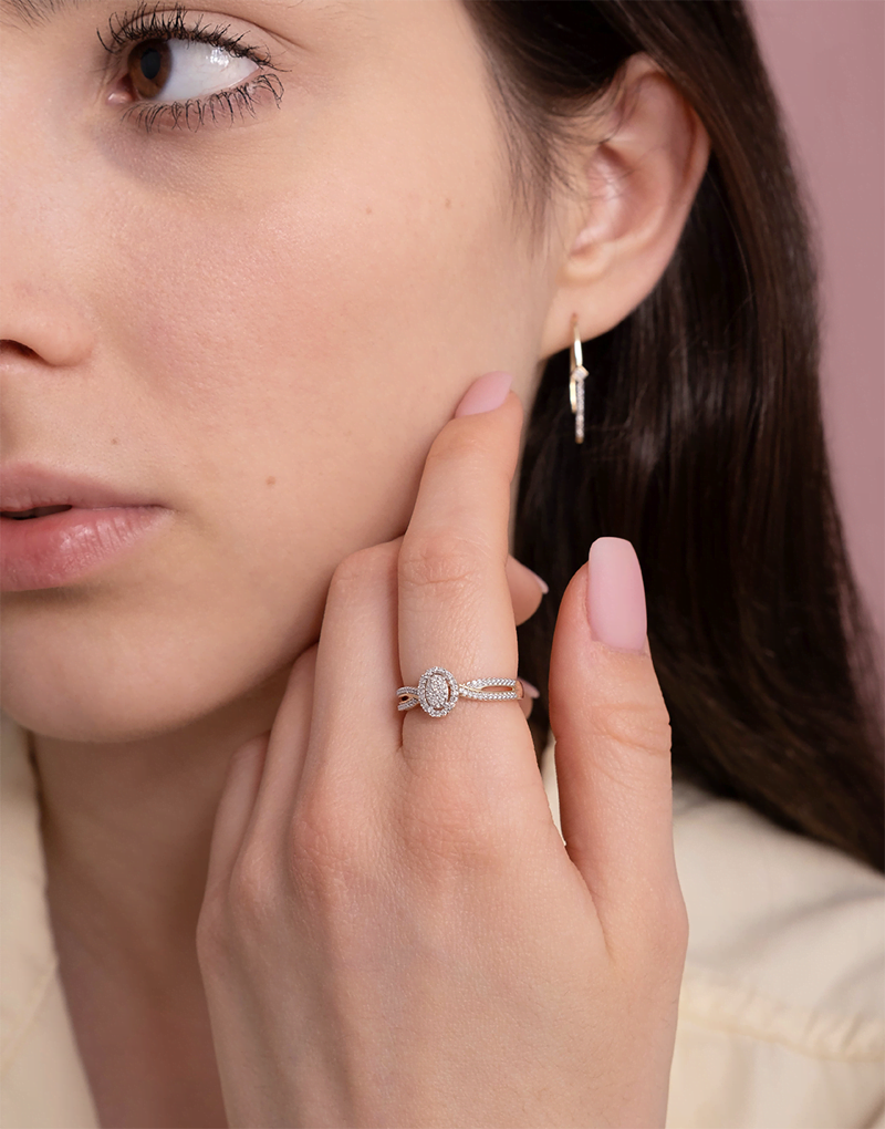 Elegancki Złoty Pierścionek z Brylantami na palcu kobiety, w połączeniu z kolczykami na tle różowym