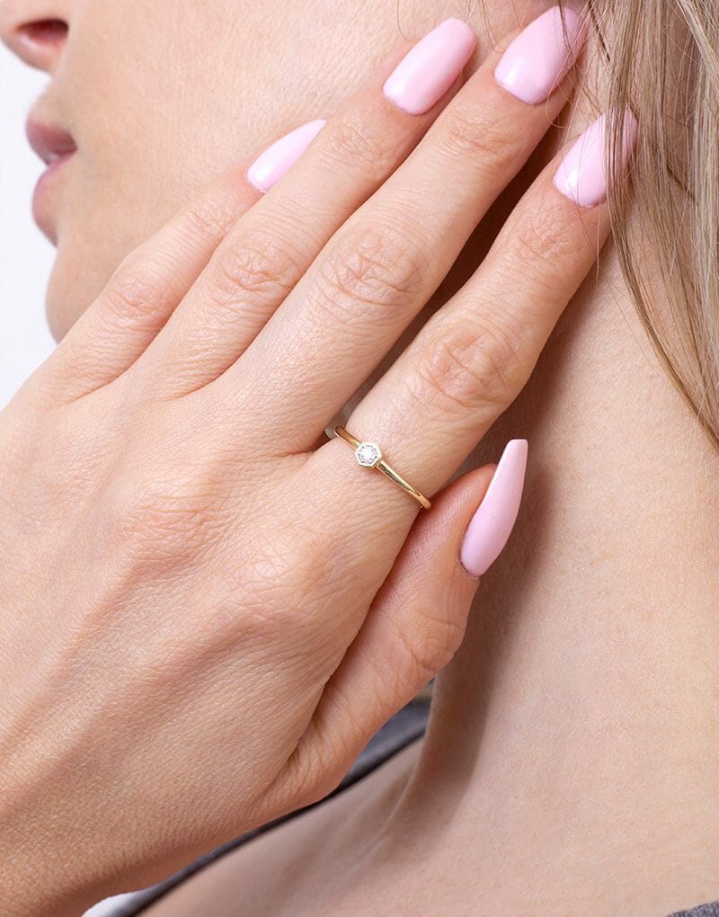 Złoty pierścionek z brylantem na delikatnym palcu z różowymi paznokciami