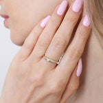 Kobieta nosi złoty pierścionek z pół-paskami brylantów na palcu, z różowym manicure