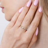 Kobieta nosi złoty pierścionek z pół-paskami brylantów na palcu, z różowym manicure