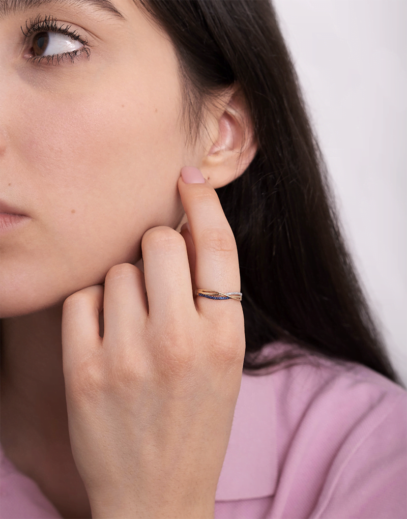 Złoty pierścionek z szafirami na palcu modelki w bluzce różowej