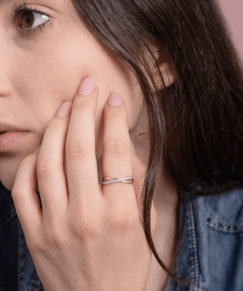 Skręcony pierścionek z brylantami od Venetia Jewels na palcu modelki, w subtelnym otoczeniu