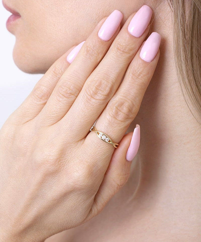 Skręcony złoty pierścionek od Venetia Jewels na dłoni z różowymi paznokciami