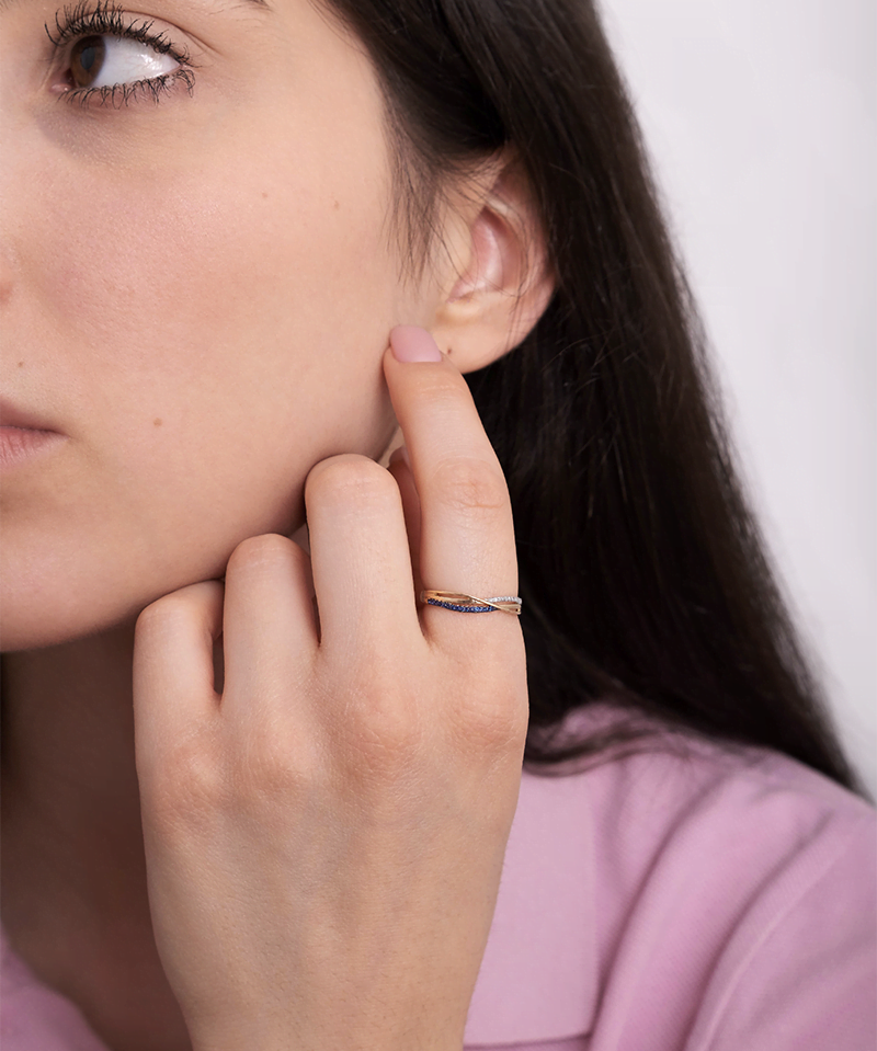 Złoty pierścionek z szafirami na palcu modelki w bluzce różowej